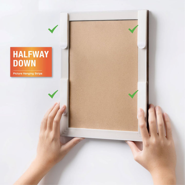 The back corners of the picture frame are attached with picture hanging strips, while both hands hold the frame to demonstrate how to use the picture hanging strips.
